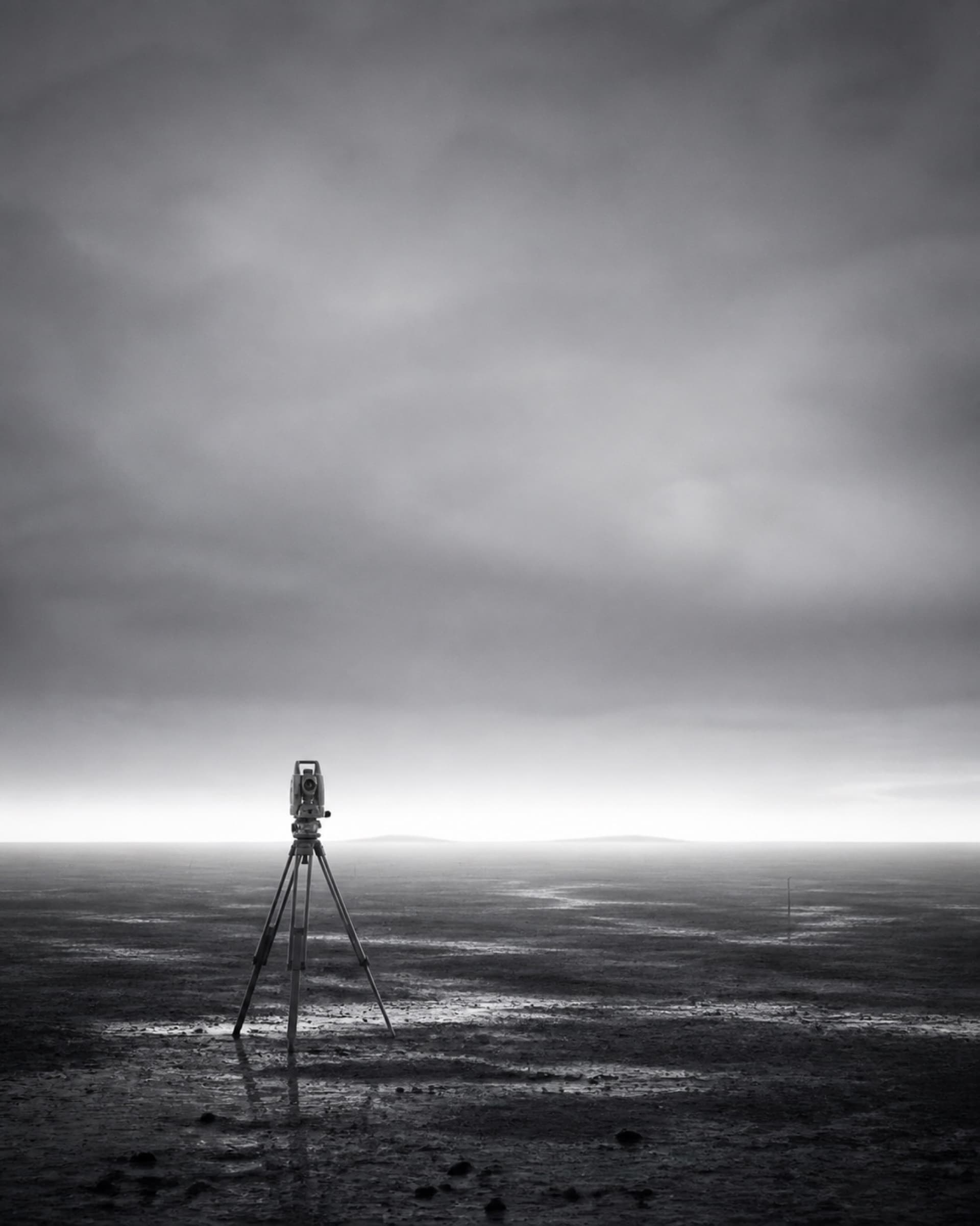 A surveyor's tripod standing on open ground in early light.