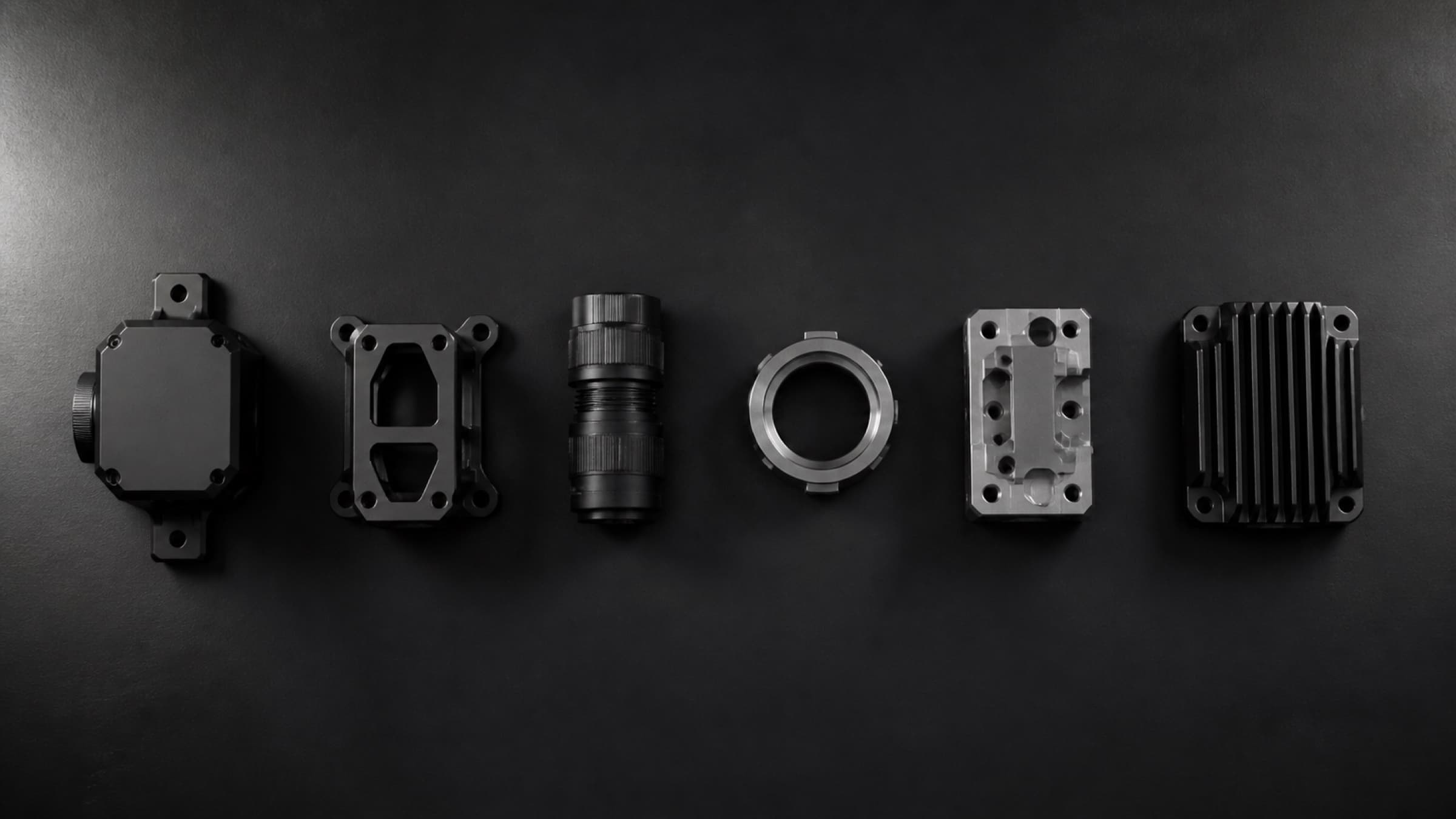Several machined components laid out in a row on a dark surface.